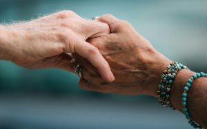 Foto på två äldre transpersoners händer som håller varandra.