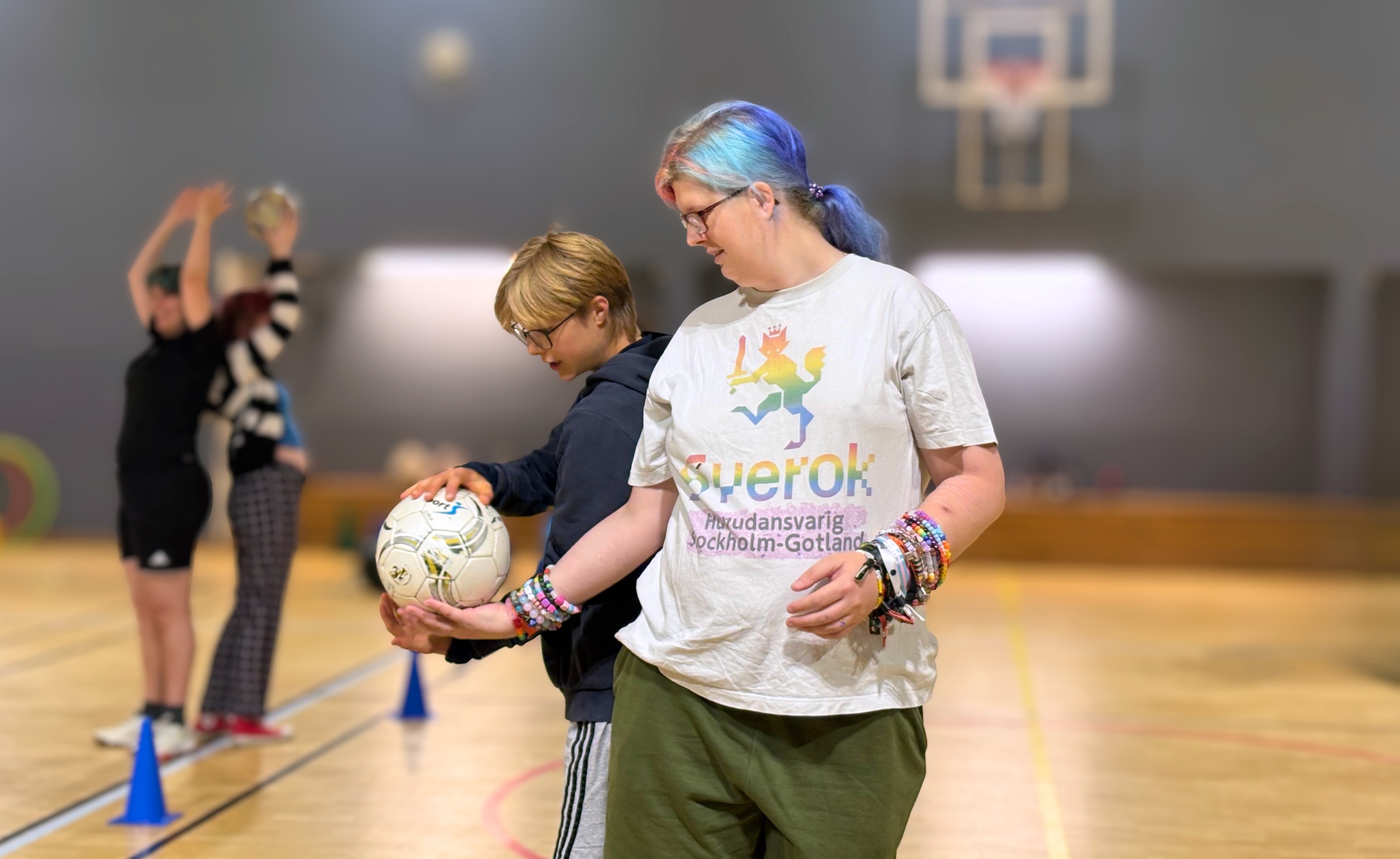 Foto på fyra transpersoner som gör en parasport övning. Två personer syns i förgrunden, de passar en boll mellan sig och är fokuserade. I bakgrunden är två andra som också passar en boll mellan sig.